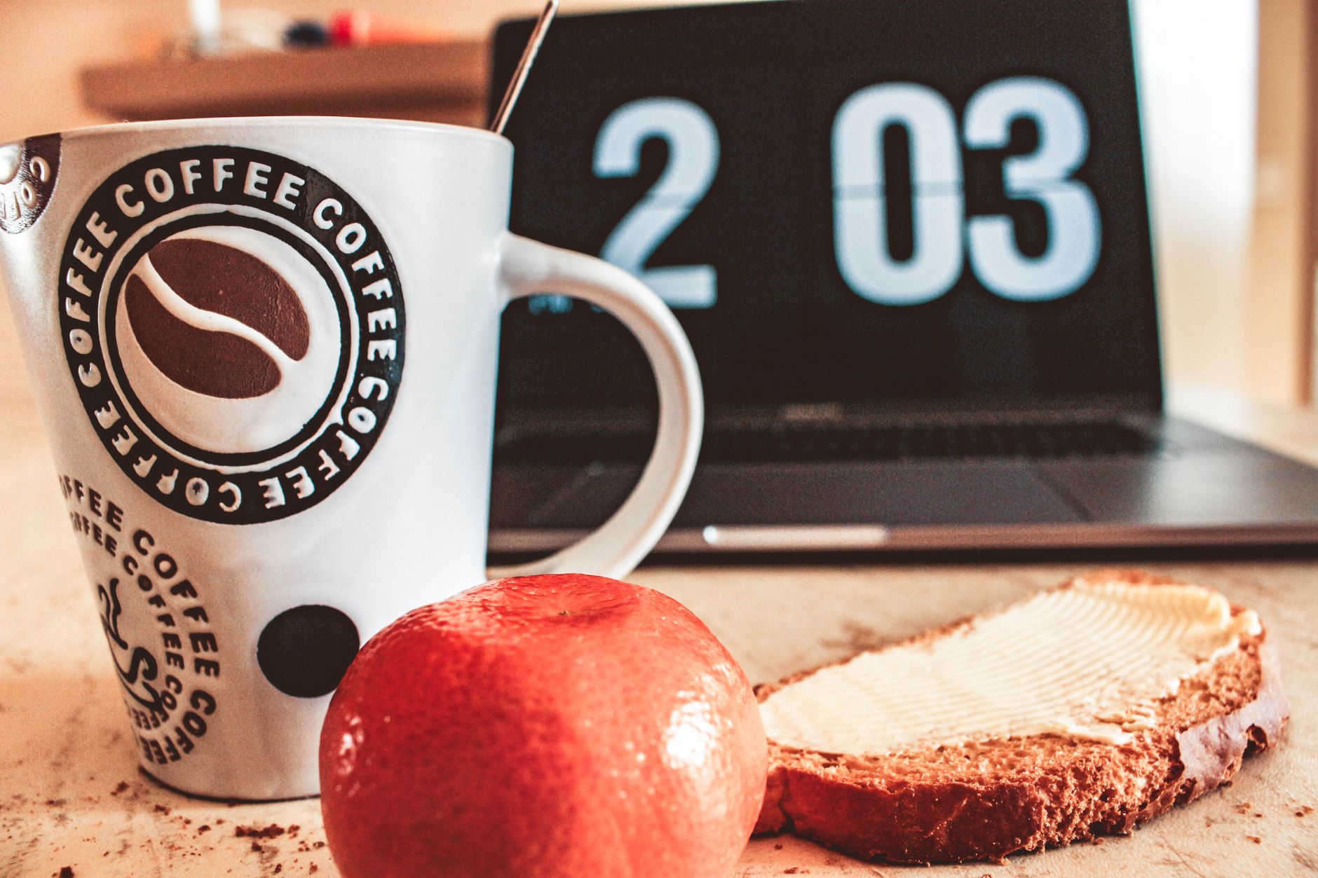 Ein gemütlicher Frühstückstisch mit Kaffee, Brot und Früchten neben einem Laptop.