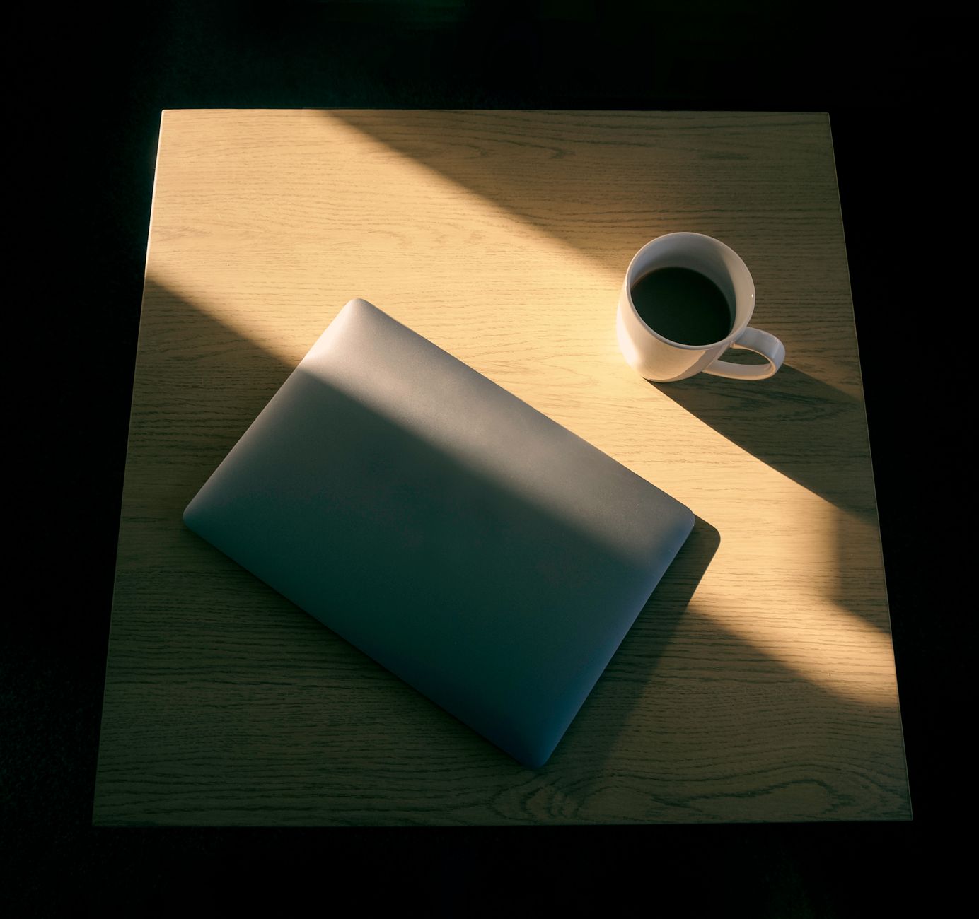 Minimalistischer Arbeitsplatz mit Laptop und Kaffeetasse im Licht- und Schattenspiel.